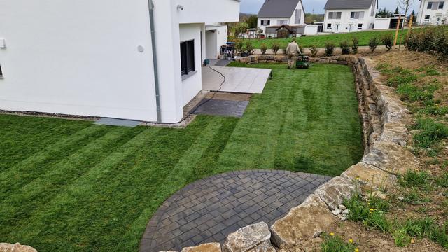 Rasenanlage mit Natursteinmauer und Pflasterrondell