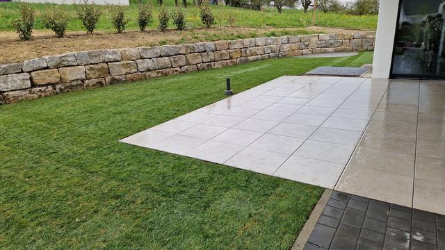 Terrasse aus Großformatplatten mit Natursteinmauer